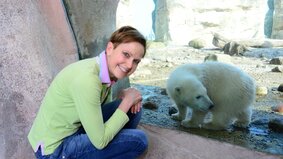 Ein Frau kniet vor einer Scheibe, dahinter befindet sich ein Eisbär. | © Zoo am Meer