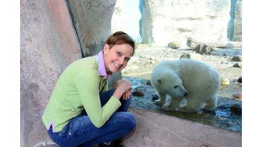 Ein Frau kniet vor einer Scheibe, dahinter befindet sich ein Eisbär. | © Zoo am Meer