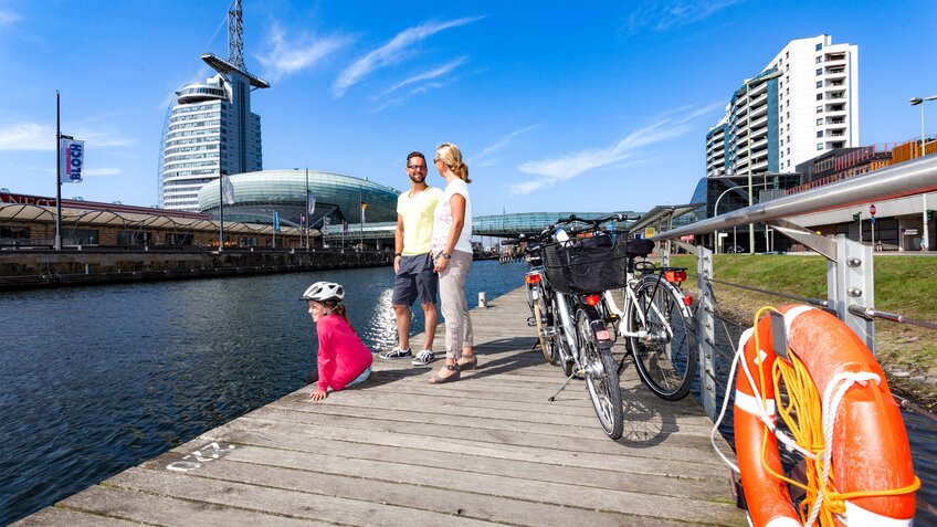 Zwei Erwachsene und ein Kind stehen auf einem Steg am Wasser, daneben stehe ihr Fahrräder. | © Helmut Gross / Erlebnis Bremerhaven GmbH