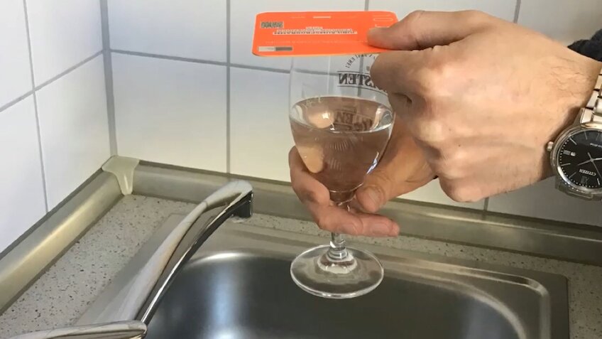 Eine Hand hält auf ein mit Wasser befülltes Glas einen orangenen Bierdeckel.  | © Sven Passarge