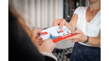 Eine Dame übergibt einer anderen Dame einen Stadtgutschein. | © Arndt Hartmann