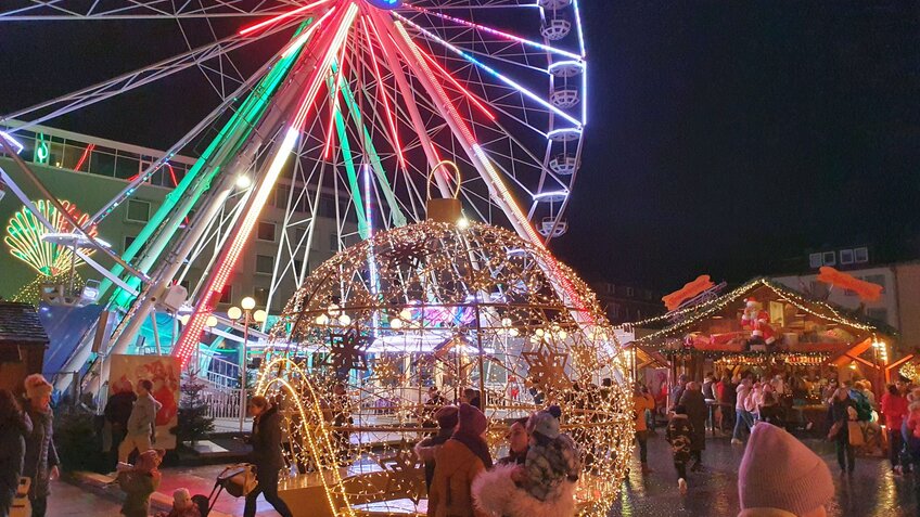 Eine Fotoaufnahme auf einem Weihnachtsmarkt am Abend mit beleuchteten Riesenrad und Lichtelementen.  | © Tanja Mehl