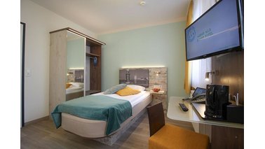 Ein Einzelzimmer mit Bett, Kleiderschrank und Fernseher im City-Hotel-Bremerhaven