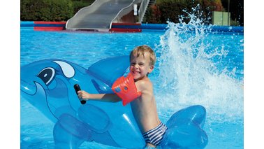 Ein Kleinkind sitzt auf seinem Schwimmtier in einem Schwimmbecken.