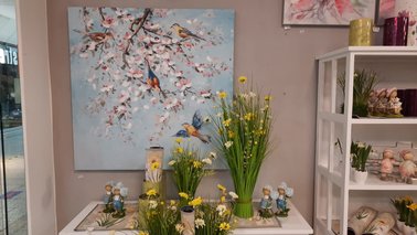 Ein Bild an einer Wand und mehrere Gestecke Blumen